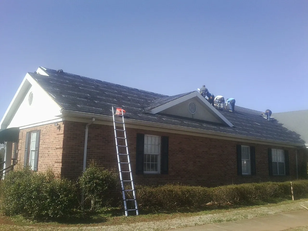 Crew tearing shingles off a brick ranch roof with a ladder set — Emergency Roof Repair work by our crew in Xenia