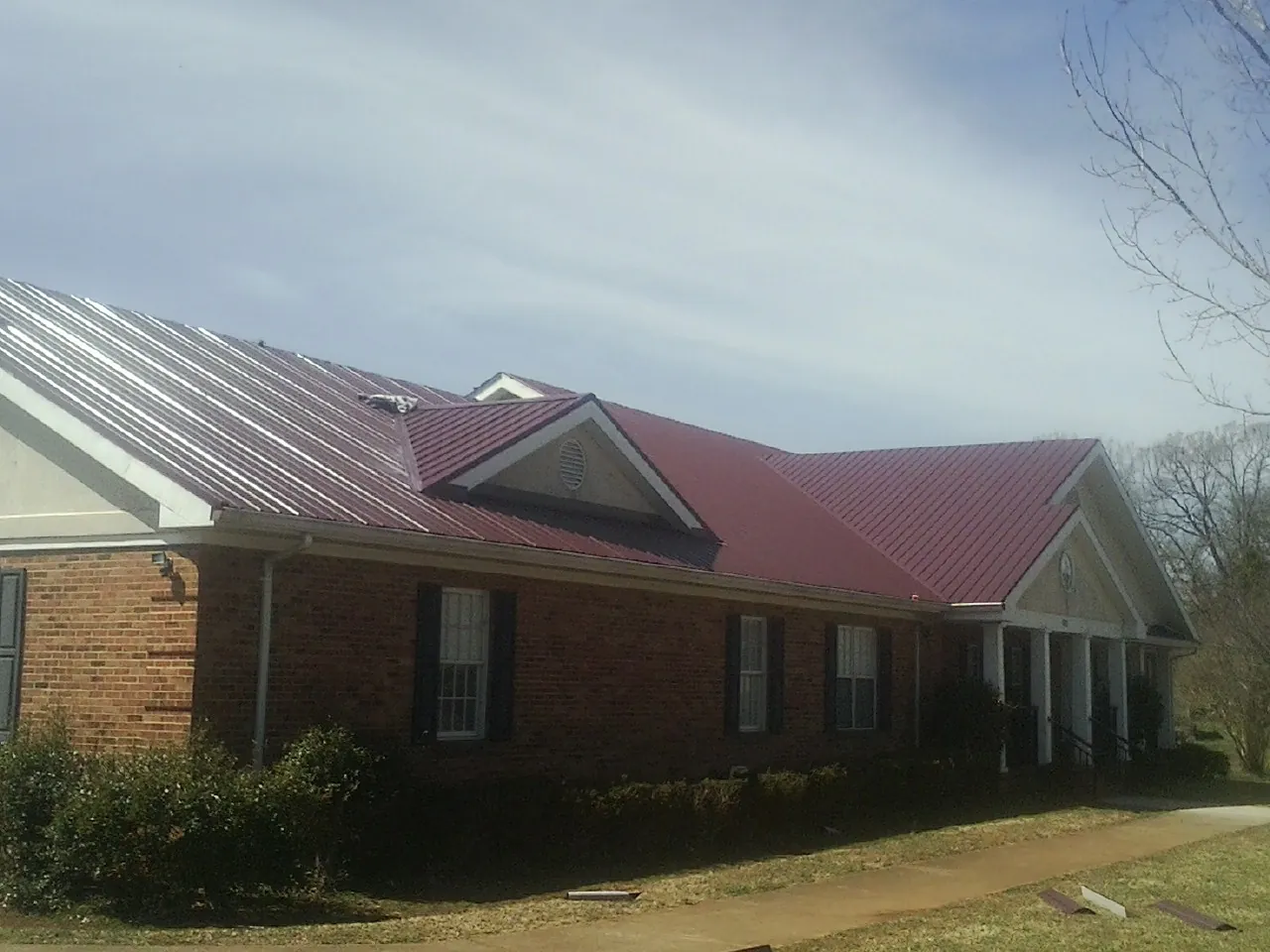 Red metal roof with gabled entries on a long brick building, from a Hail Damage Roof Repair job in Xenia