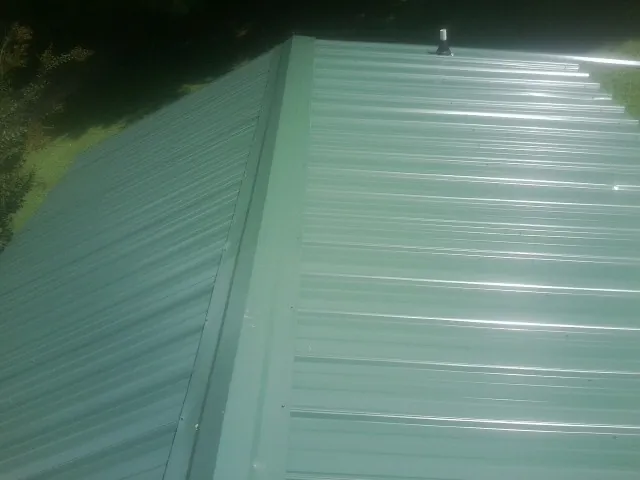 New green metal panels meeting at the ridge of a roof — Flat Roof Repair work by our crew in Xenia