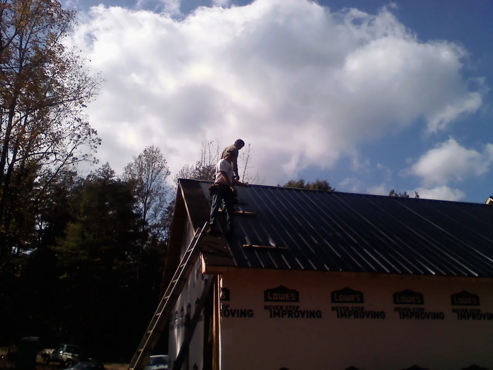 Roofer fastening dark metal panels high against a cloudy sky, from a Roof Inspection job in Xenia
