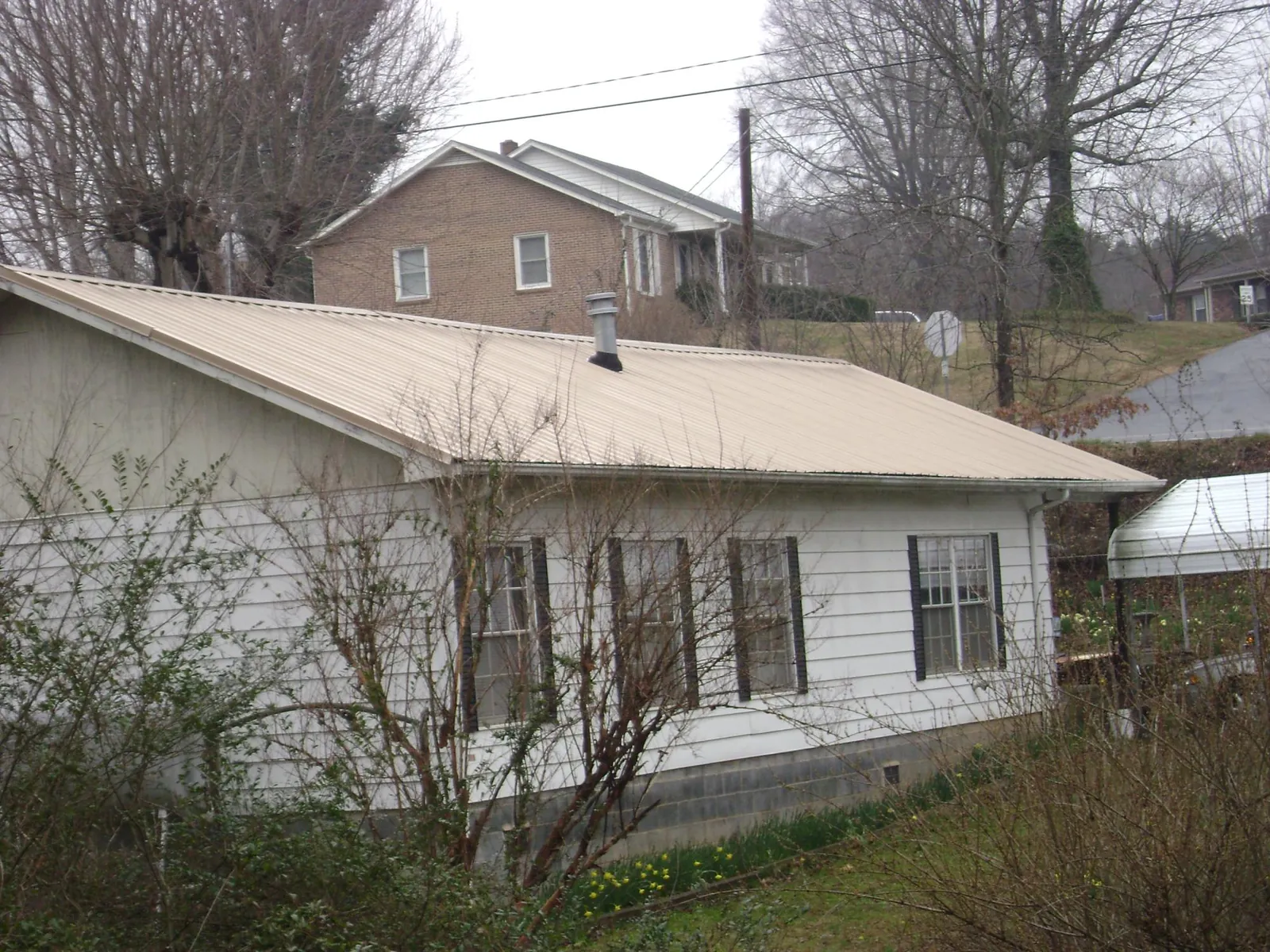 Tan metal roof on a white sided house set into a hillside — Commercial Roofing by Roofing Brothers in Xenia